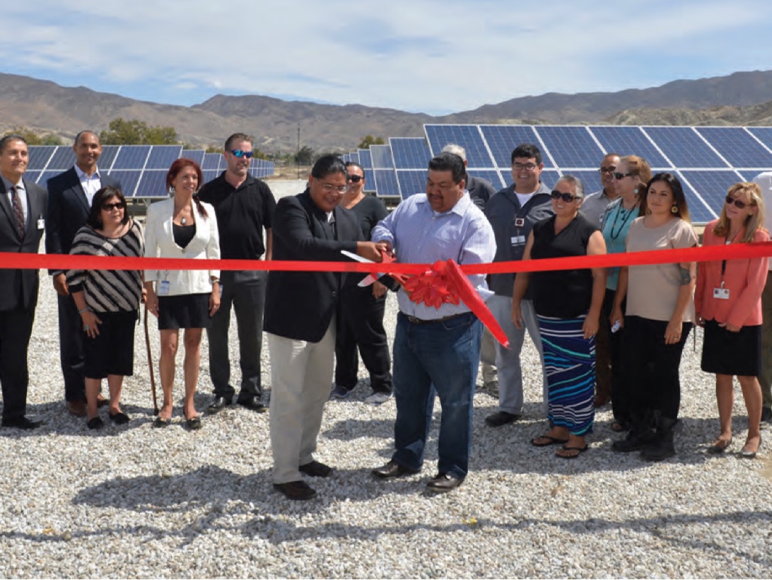Ribbon cutting with a group of people  outside, in front of solar panels.