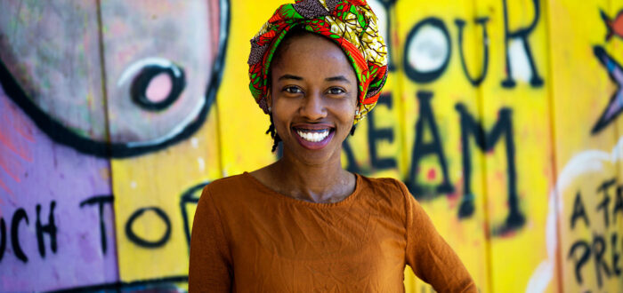 Black woman standing in front of a colorful mural, smiling