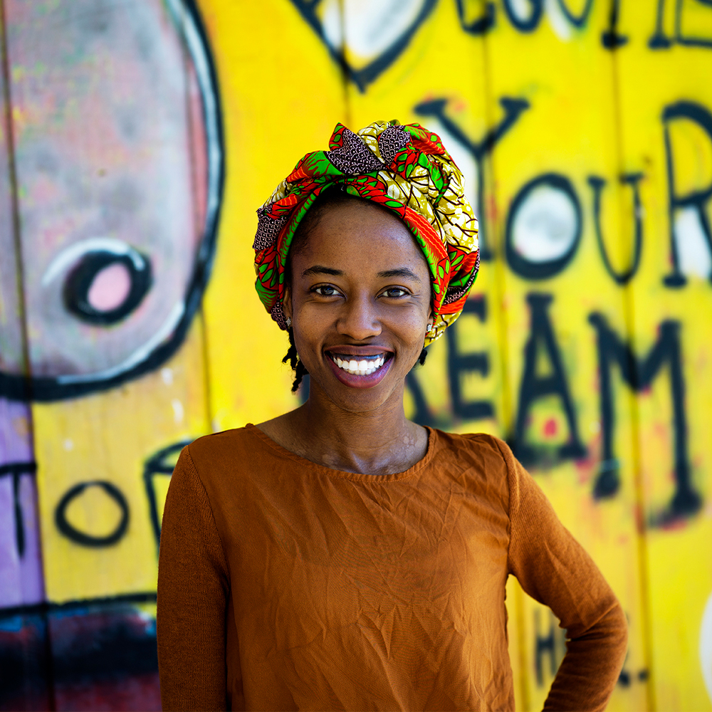 Black woman standing in front of a colorful mural, smiling