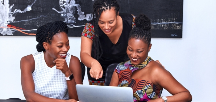 three Black women gathered around a computer excited with smiles as they review the content