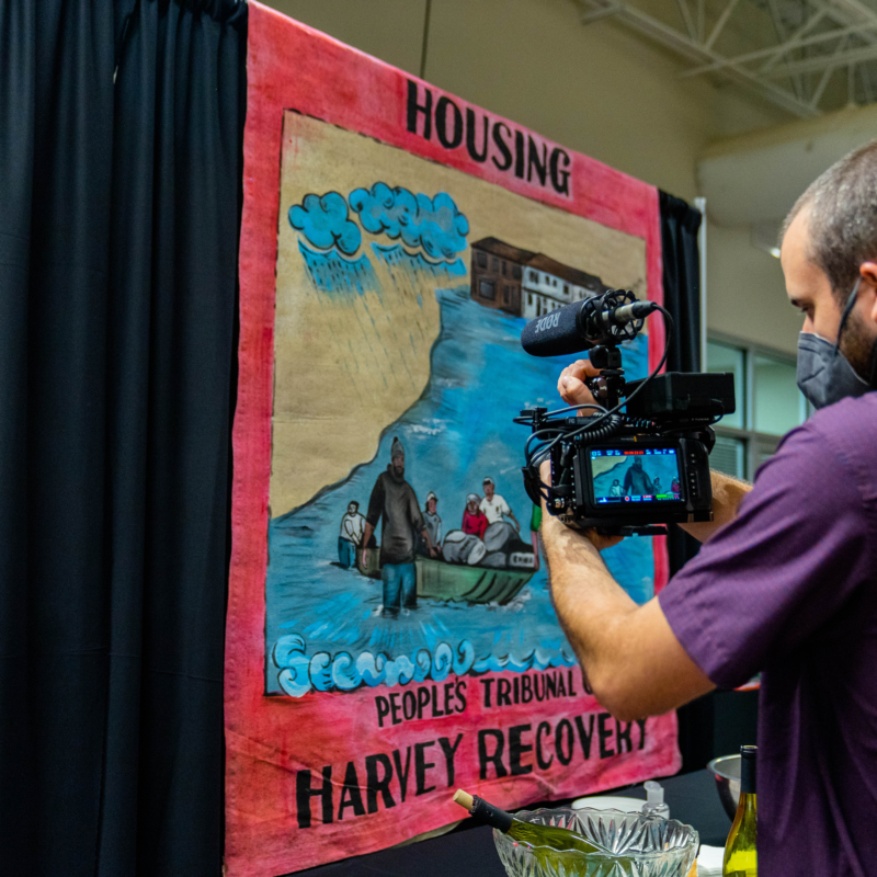 man in purple shirt with a video camera taking video of the Housing Harvey Recovery artwork