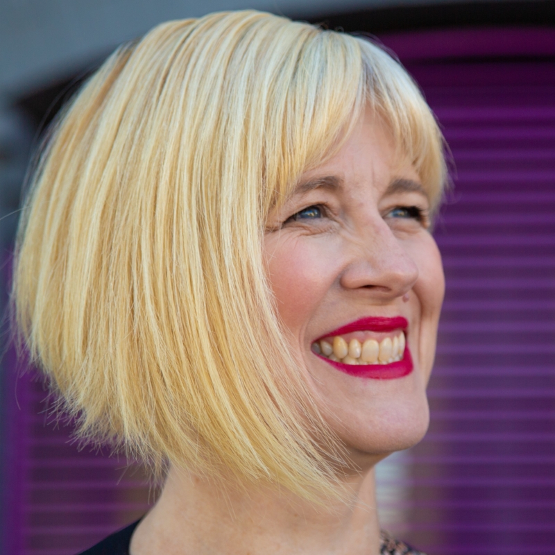 Woman who appears to be white with short blonde hair and red lipstick smiling