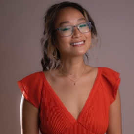 Young woman who appears to be Asian, with glasses in a red vneck dress with ruffle sleeves smiling
