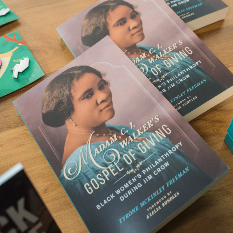 photo of the cover of Madam C.J. Walkers Gospel of Giving book which depicts a Black women (Madam C.J.) appearing to sit for a photo shoot